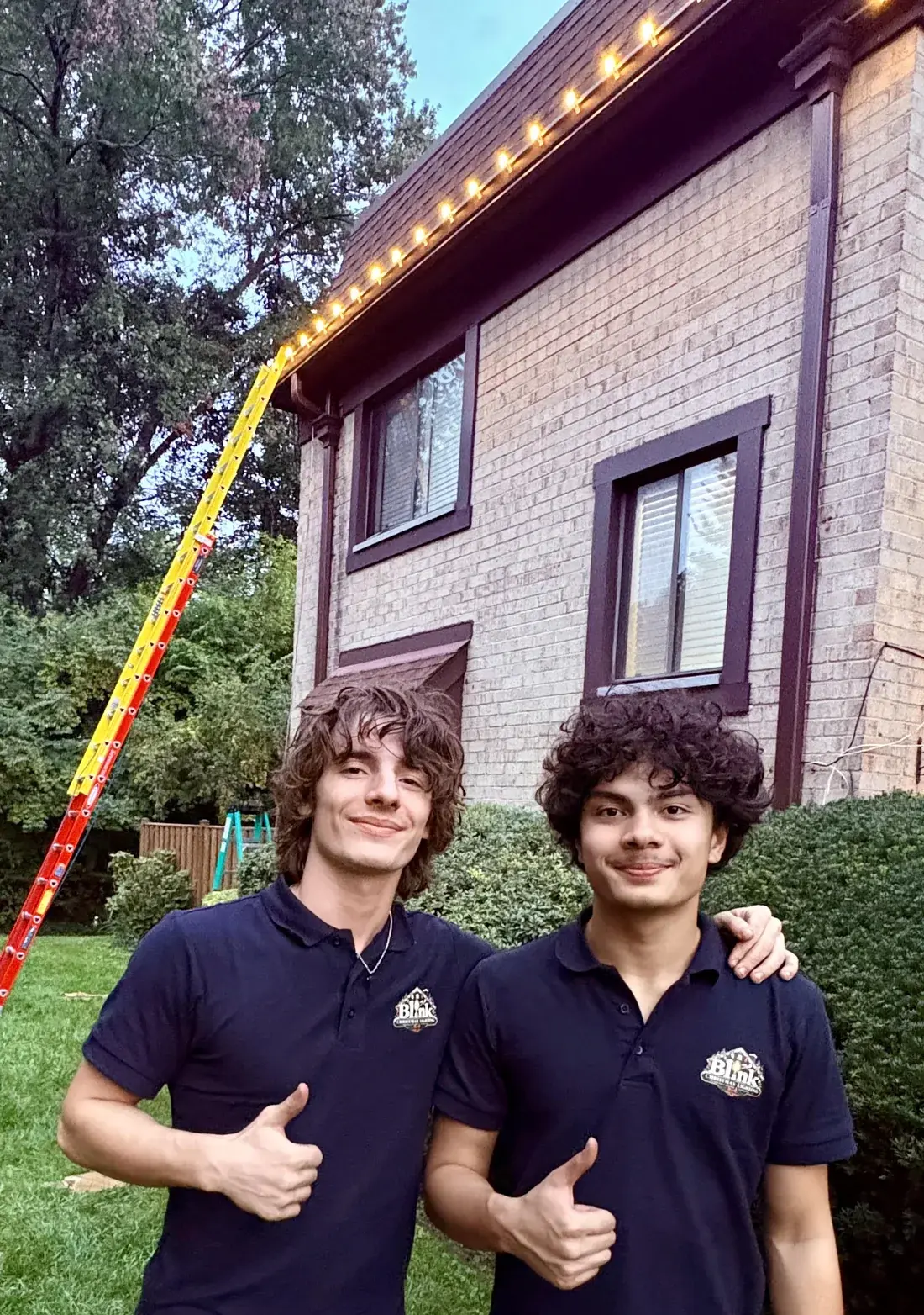 Two members of the Blink crew in Blink polos, giving a thumbs up under a freshly lit roofline.