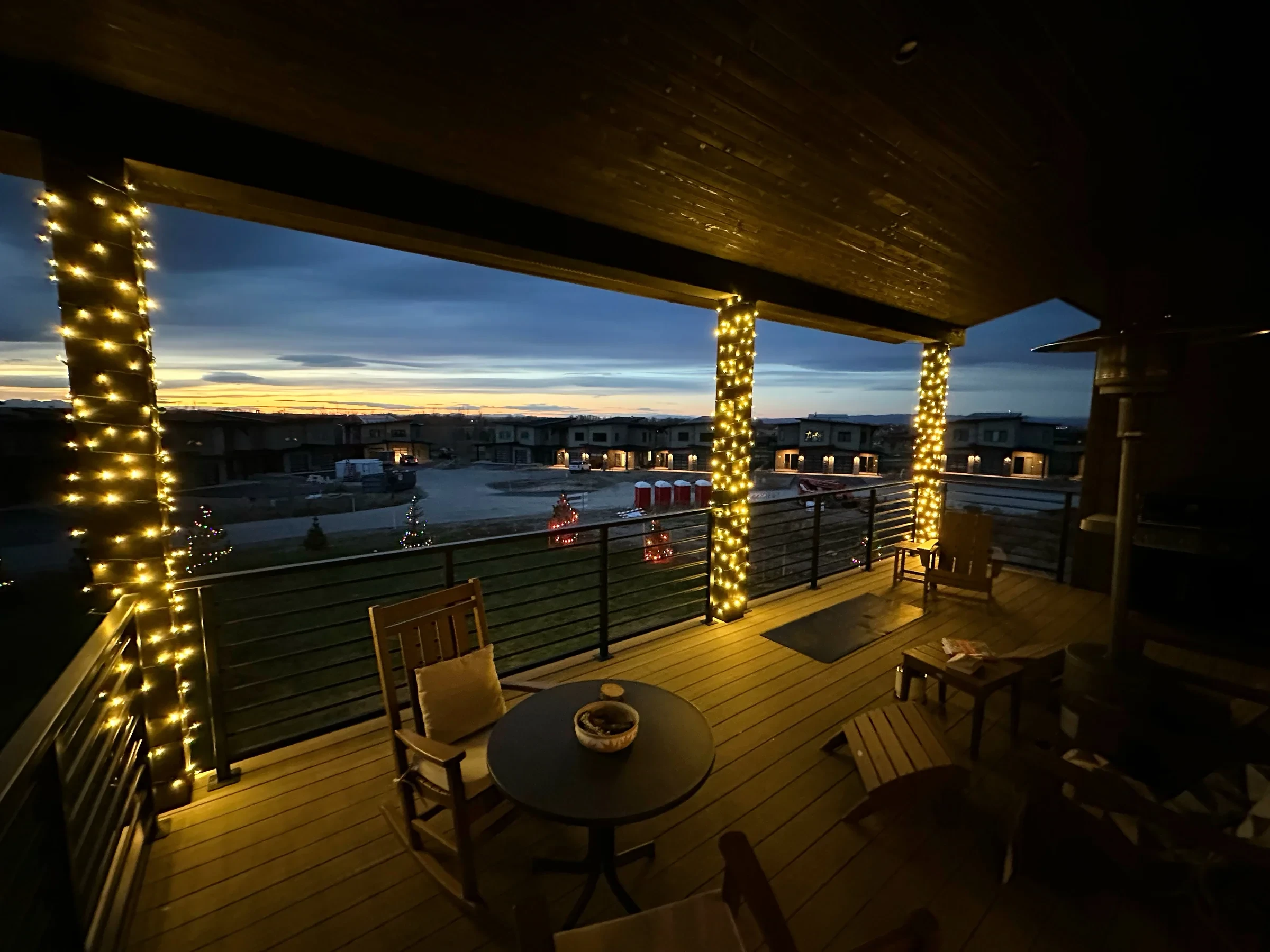 Covered deck with columns wrapped in warm white lights at sunset.