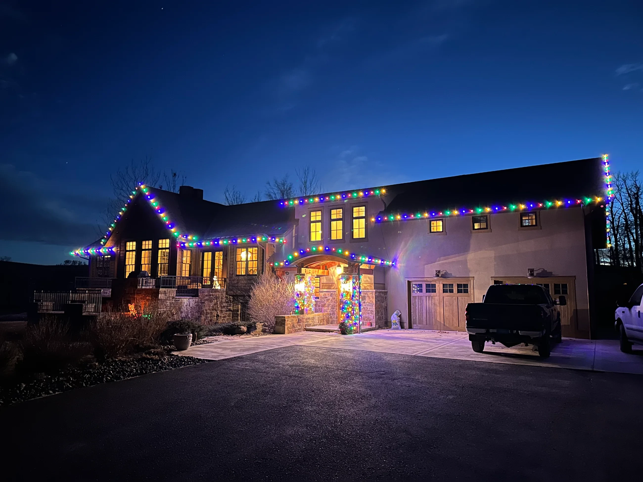 Large home with multicolor Christmas lights along the roofline at dusk.