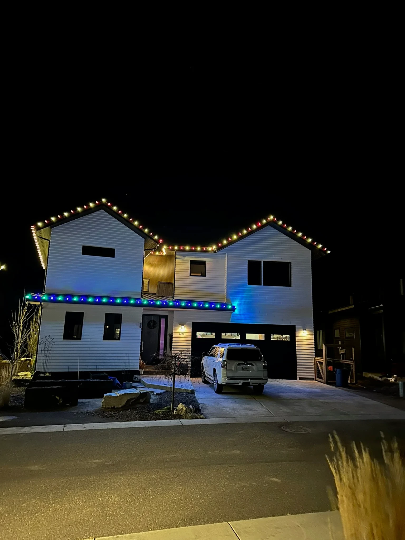 Two-story home with red and warm white lights on the upper rooflines and blue and green below.