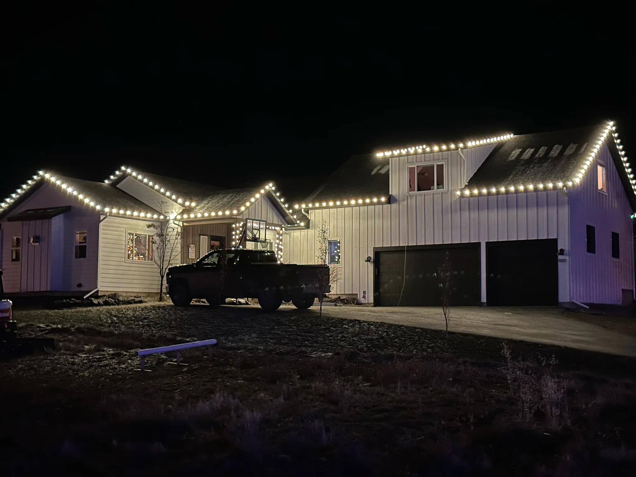 Modern farmhouse with a three-car garage outlined in bright white roofline lights.