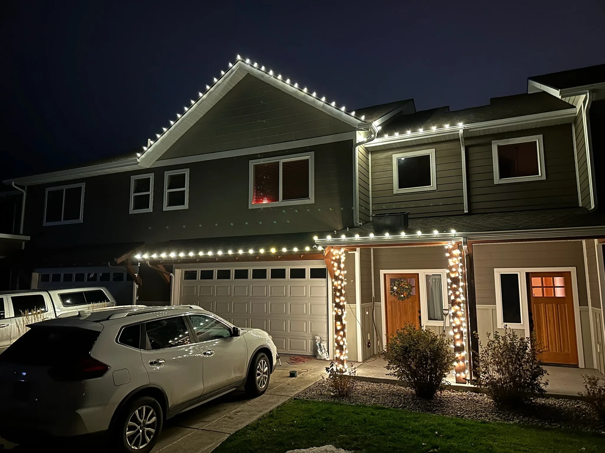 Two-story home with white Christmas lights on each roofline and wrapped porch pillars.